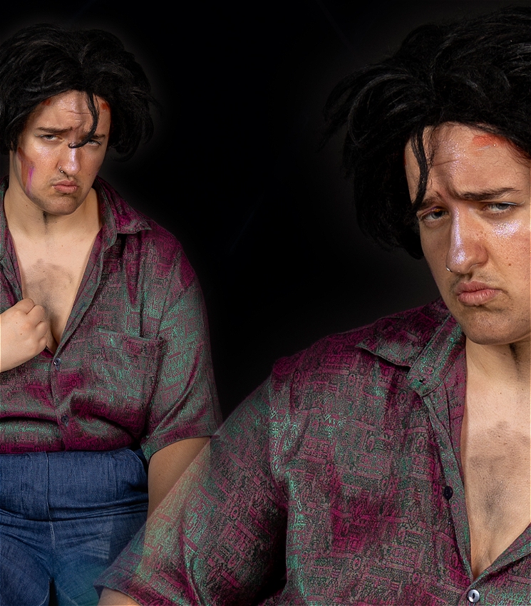 Two images of Silvio Di Baci, a caucasian drag king, looking at the camera with a sultry look on his face - similar to a 80s glamour shot. He is wearing blue trousers and a glistening purple and cyan shirt that is partially unbuttoned. He has thick black hair and his face is covered in pink glitter, with some orange paint marks. In the left image, he strikes a model pose holding his shirt collar open. Whereas on the right, he glances his side-eye away from the viewer, sitting with poise.