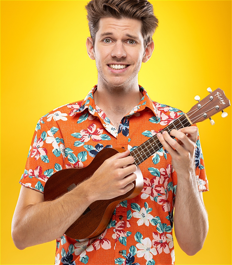 A portrait of a man wearing a bright orange Hawaiian shirt and wielding a Ukulele in front of a bright yellow background. He's smiling but his eyes look very concerned.