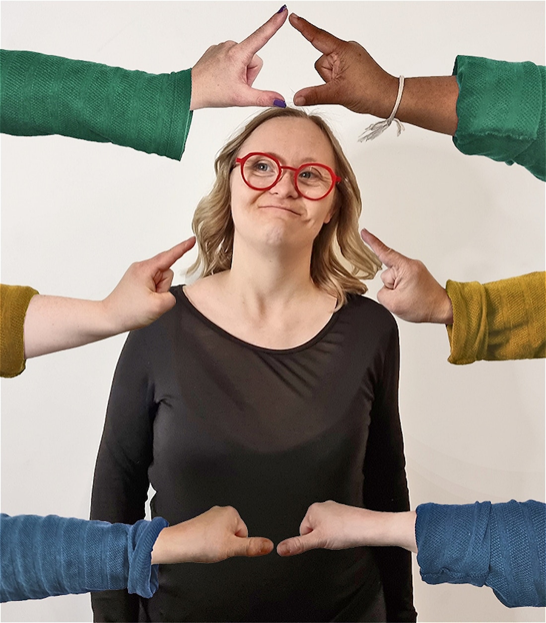 A woman with Down syndrome and blonde shoulder length hair in a black top and red glasses, smiling thoughtfully. 3 arms reach from outside of the frame on each side making different shapes with the hands framing the womans face and body.