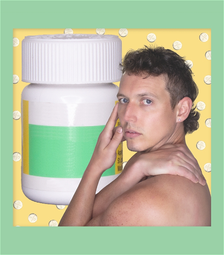 The performer is shirtless with body faced away from the camera, looking into the lens holding a modelling pose with hands near the face. Behind them is a cut out pill bottle and small yellow pills strewn across the image.