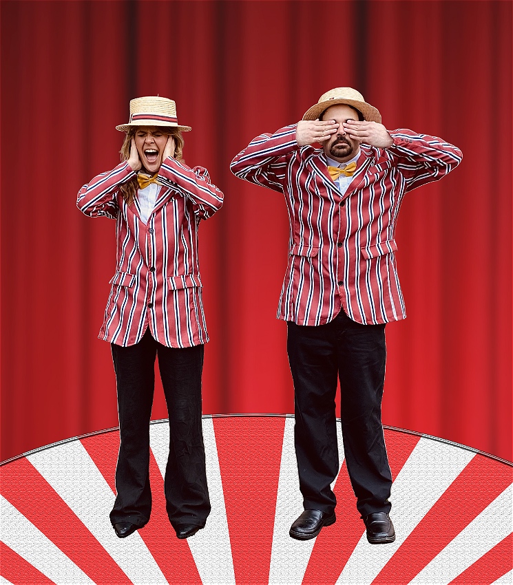 A woman screams while covering her ears, beside a man covering his eyes with his hands, reminiscent of 'hear no evil, see no evil'. They wear matching red and white striped suits with yellow bowties and straw flat hats. They stand in a spotlight in front of red curtains, atop a red and white circus platform.