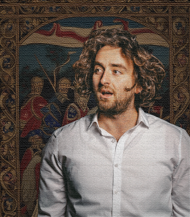 A man in a white shirt and shaggy brown/blonde hair standing in a front of a medieval themed tapestry. A digital tapestry effect is over him so it looks like he's part of the artwork.