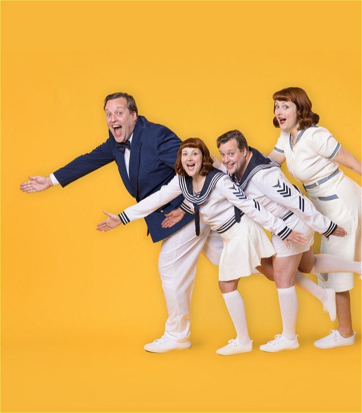 Four people are posing in a playful manner against a bright yellow background, as if all dancing in unison. The two women and two men are dressed in nautical-themed outfits. One man is in a blue suit, while the others are wearing white sailor uniforms. They are all smiling and leaning forward with their arms outstretched, creating a dynamic and lively group pose.