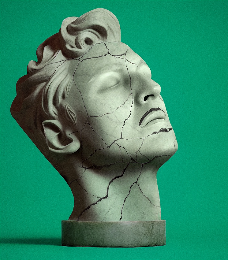 A marble statue of a man's head, badly cracked, in front of a green background. The face has a moustache drawn onto it in marker.