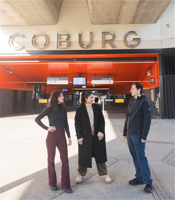 This image features three people standing outside a building with a large sign that reads 