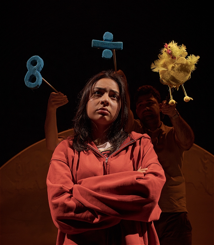 A young women in a red hoodie and crossed arms stands deep in thought. Puppets of numbers and a chicken float above her.