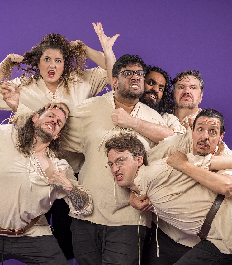 The image features seven people jostling against a purple background, to be in the frame. They are all dressed in similar off-white shirts, and their expressions and body language are exaggerated, conveying a sense of fun and chaos. Some are pulling at their shirts or making animated gestures.