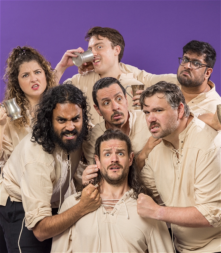 The image features the same group of seven people against a purple background. They are all dressed in similar off-white shirts and holding metal mugs, some appearing to drink from them. A Some characters are threatening a player in the middle and pinching his ear. It's a comedic picture.