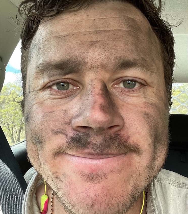 Close up of a man's face staring into camera with grease and dirt on face. He is sitting in his car.