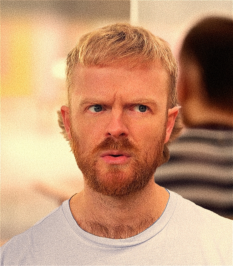 The image features Lukas Meintjes with a puzzled expression. He is looking slightly off camera, mouth slightly open as if in mid-sentence. Lukas has light blonde hair, a trimmed beard, and is wearing a lilac t-shirt. The background is softly blurred, highlighting his facial expression.