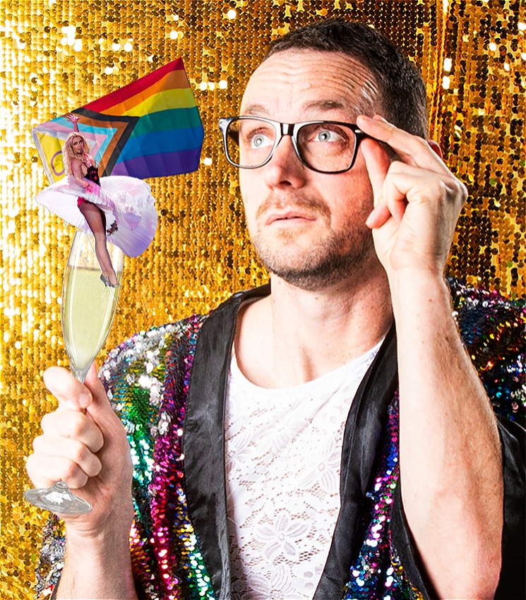 A man in a sparkly sequin coat looks up to the right, holding a champaign flute with a progressive pride flag sticking out of it, while holding onto glasses with no lenses in them