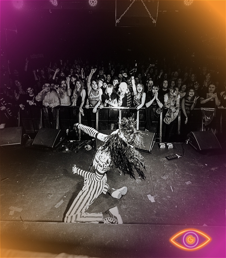 Drag King wearing black and white performing on stage.
Large crowd cheering them on.