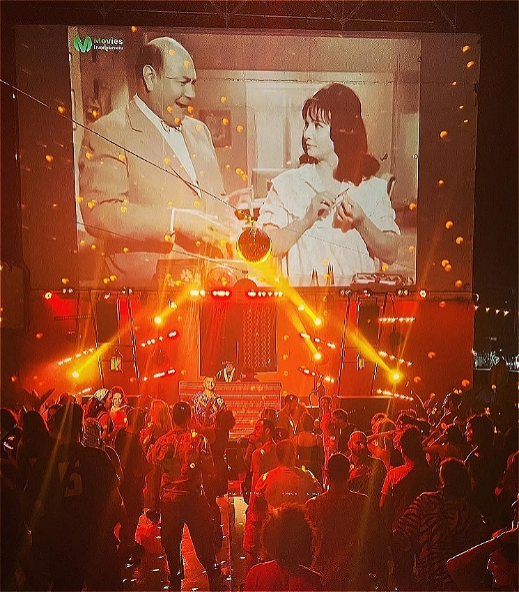 MzRizk DJing to a happy crowd of dancing people on a club rooftop.