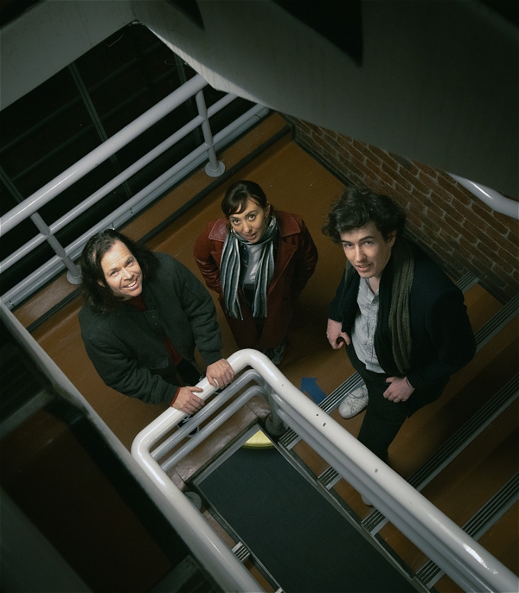 An image of musicians James Howard, Alice Sky and Michael Julian standing together in a stairwell looking upwards