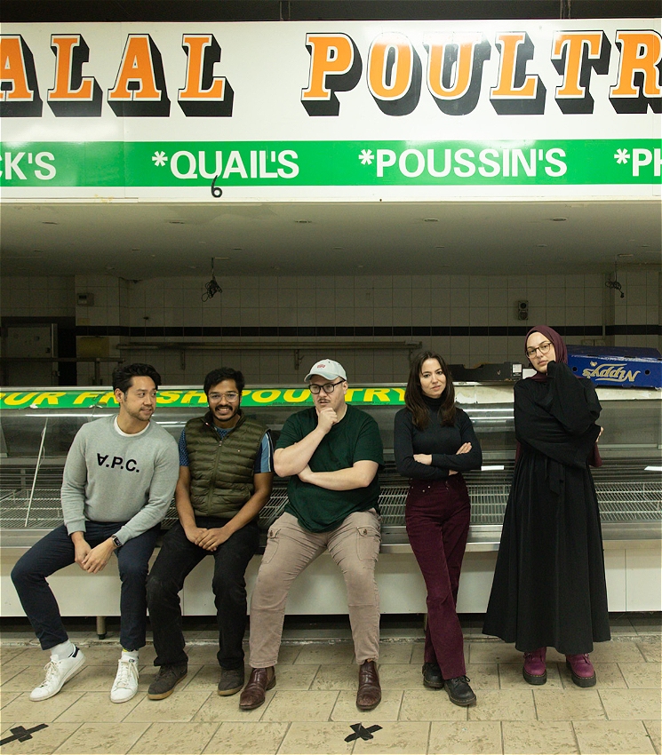 Five people (two women and three men) are leaning against a vacant butcher's cabinet. They appear laidback, cool and calm. They are looking into the camera.