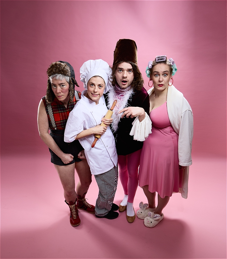 A wide-angle image of 4 caucasian people, standing side-to-side in a vibrant pink background. They are dressed in different outfit, donning different hats and wearing dramatic facial expressions, while staring straight at the image source.