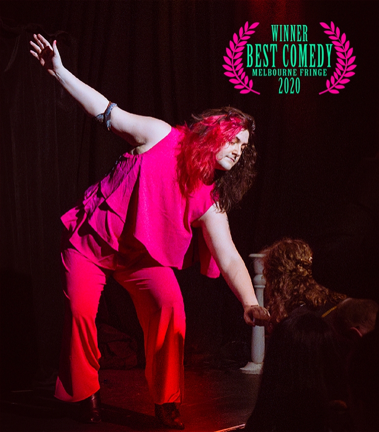 An image of tricksy standing in a bright pink outfit on stage, against dark red velvet curtain in the centre of a spotlight. Her right arm is stretched and raised to her side, as she bows offering her left hand to a patron to inspect. In the top right corner, is an award laurel that reads 