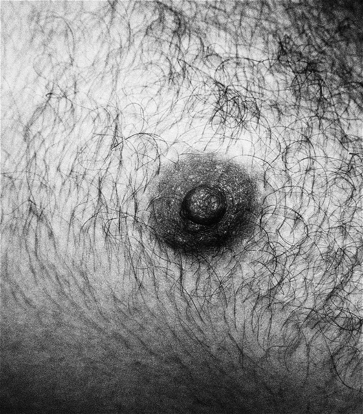 A close-up black and white image of a nipple, surrounded by chest hair