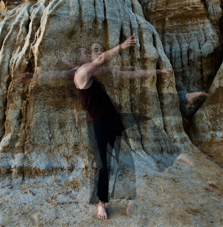 Female acrobat mid motion, photographed in triple exposure, wearing all black, background is earthy yellow sandstone cliffs.