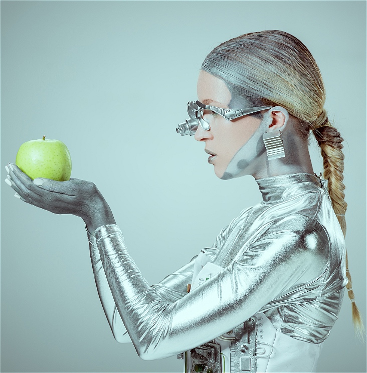 Side view of cyborg holding and examining green apple isolated on grey, future technology concept, 2021.