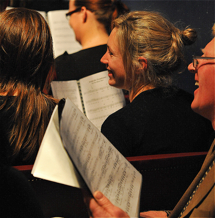 Two people singing holding sheet music and smiling.