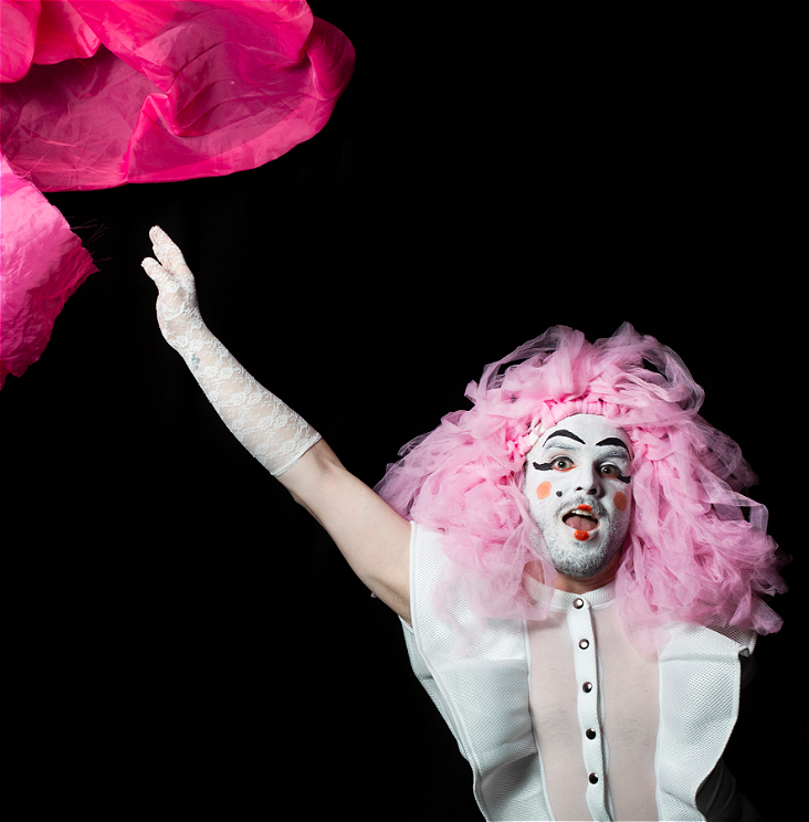 A person in white makeup and pink hair throwing a pink sheet