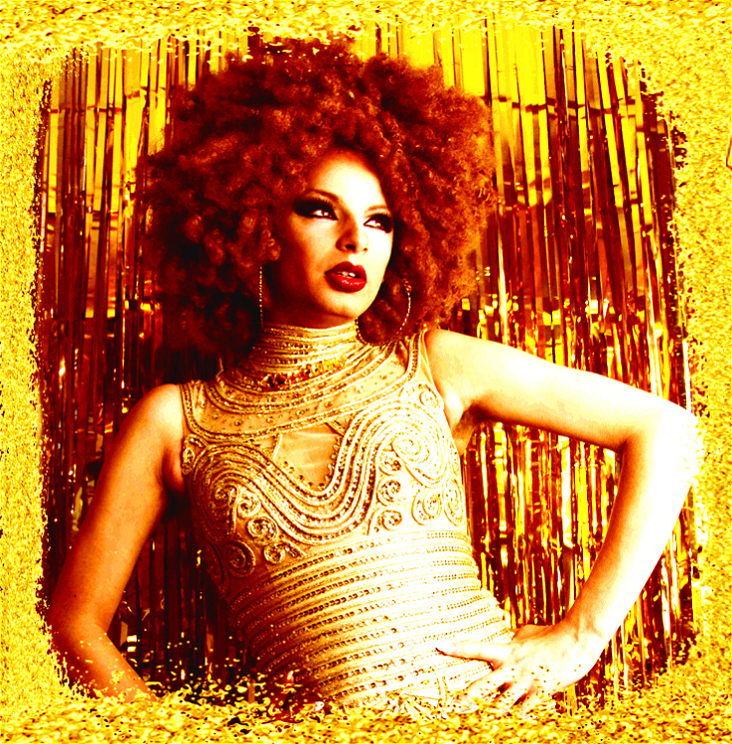 A person wearing a gold jewelled top with curly brown hair posing with arms on hips in front of a gold shimmer curtain. There is a gold wash over the image.
