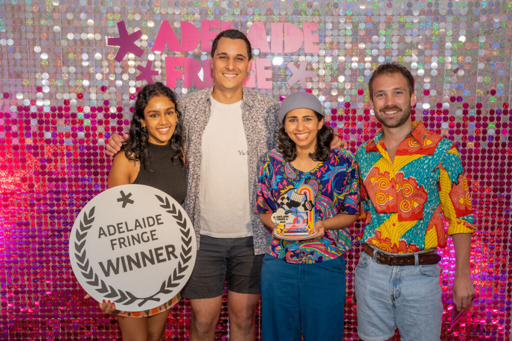 four people standing in front of a pink shimmer curtain holding an award