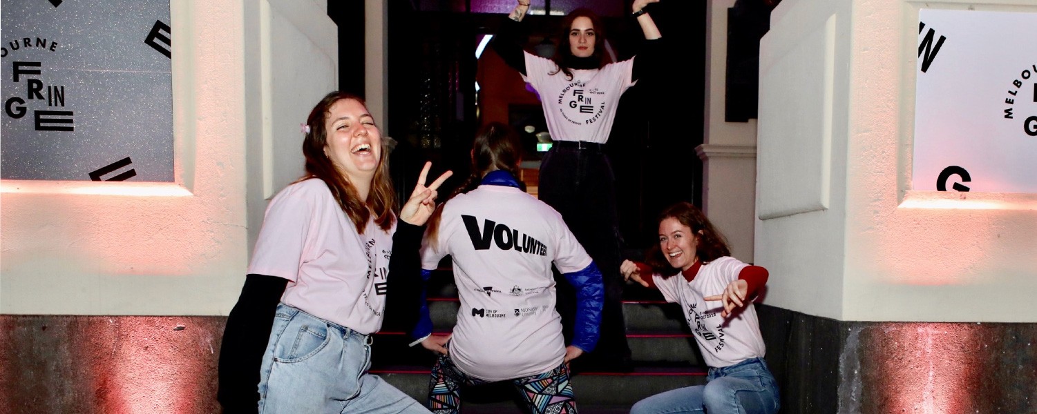 Four people crouch on the steps of a building wearing pink t shirts